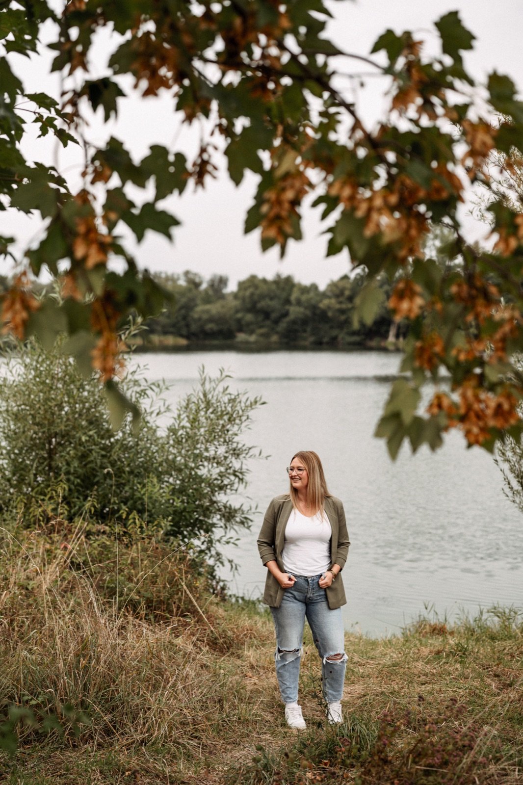 Sarah Meister am Ufer eines Sees, umrahmt von herbstlichen Zweigen
